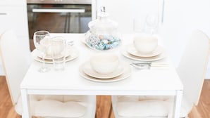 A white dining table set with plates, bowls, glasses, and cutlery.