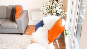 A modern living room with a grey sofa, a white chair with orange cushions, a white rug, and a wooden floor.