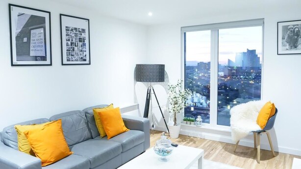 A modern living room with a grey sofa, yellow cushions, a white coffee table, and a large window offering a city view.