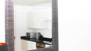 A mirror with a speckled frame reflecting a kitchen area with white cabinets and a black countertop.