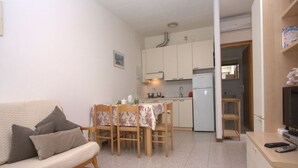 A compact living space with a sofa, dining table, chairs, a kitchenette, and a television. - Villa Capinera (Lignano Sabbiadoro)