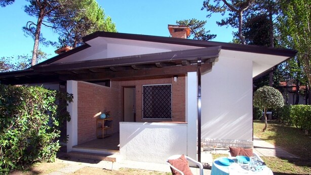 A small outdoor patio with a table and chairs, a brick wall, and a covered area with a window. - Villa Capinera (Lignano Sabbiadoro)