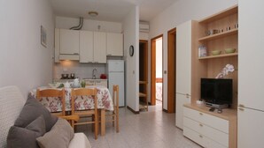 A compact living space with a kitchenette, a dining area, a TV, and a sofa. - Villa Capinera (Lignano Sabbiadoro)