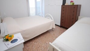 Ein Schlafzimmer mit zwei Betten, einer Holzkommode und einem kleinen Tisch mit Blumen.