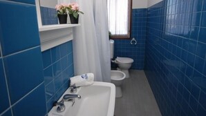 Ein Badezimmer mit blauen Fliesen, einem weißen Waschbecken, einer Toilette und einer Duschvorhang.