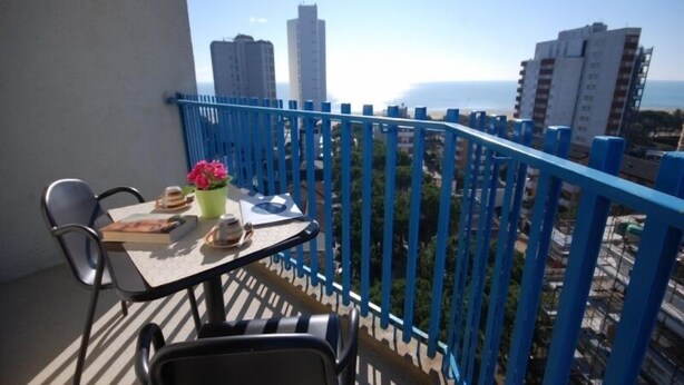 Ein Balkon mit Tisch und Stühlen, einem Blumentopf und Blick auf hohe Gebäude und das Meer.