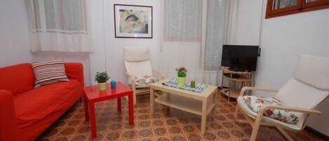 Un salón con un sofá rojo, una mesita, un televisor y un suelo estampado.
