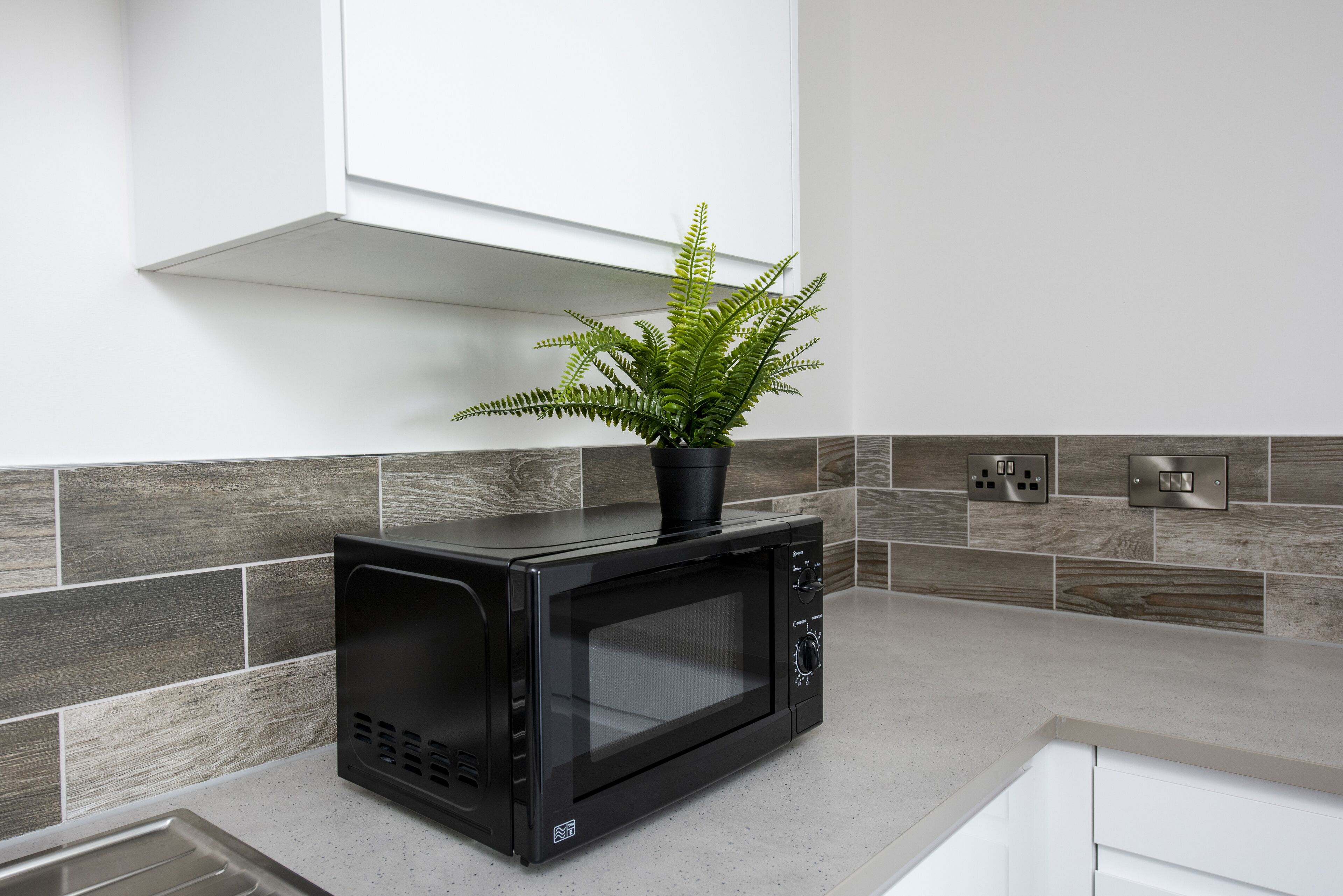 A modern kitchen with a black microwave, a potted plant, and a grey tiled backsplash.