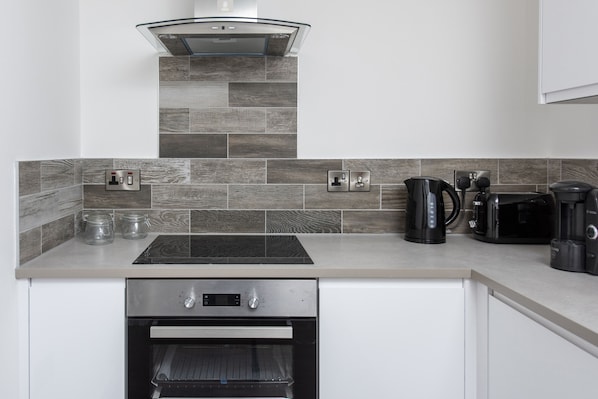 A modern kitchen with a built-in oven, a coffee maker, and a kettle on the countertop.