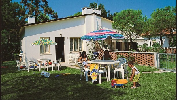 Una casa con patio, muebles de exterior y un niño jugando con un camión de juguete.