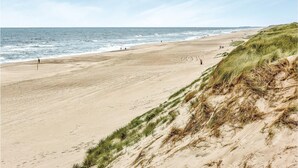 Une vaste plage de sable fin, avec des vagues douces, des dunes herbeuses et un ciel dégagé.