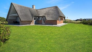 Une maison à toit de chaume, avec une base en briques, située dans un champ herbeux.