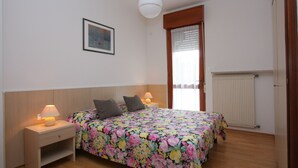 Een slaapkamer met een bed, nachtkastjes, een lamp, een radiator en een raam met gordijnen.