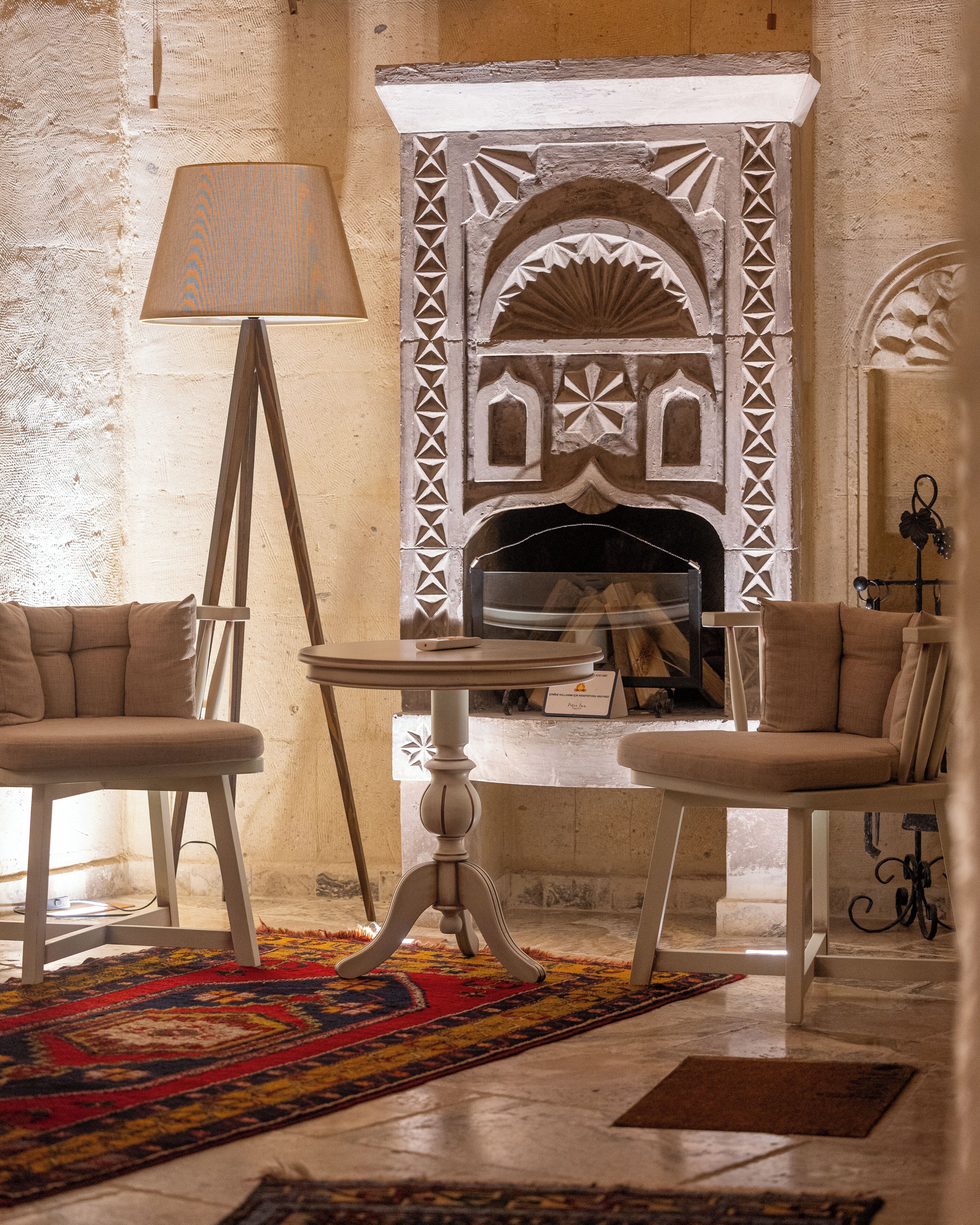 A room with a fireplace, two armchairs, a floor lamp, and a patterned rug.