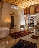 A bathroom with a bathtub, two chairs, a table, a mirror, and a patterned rug.