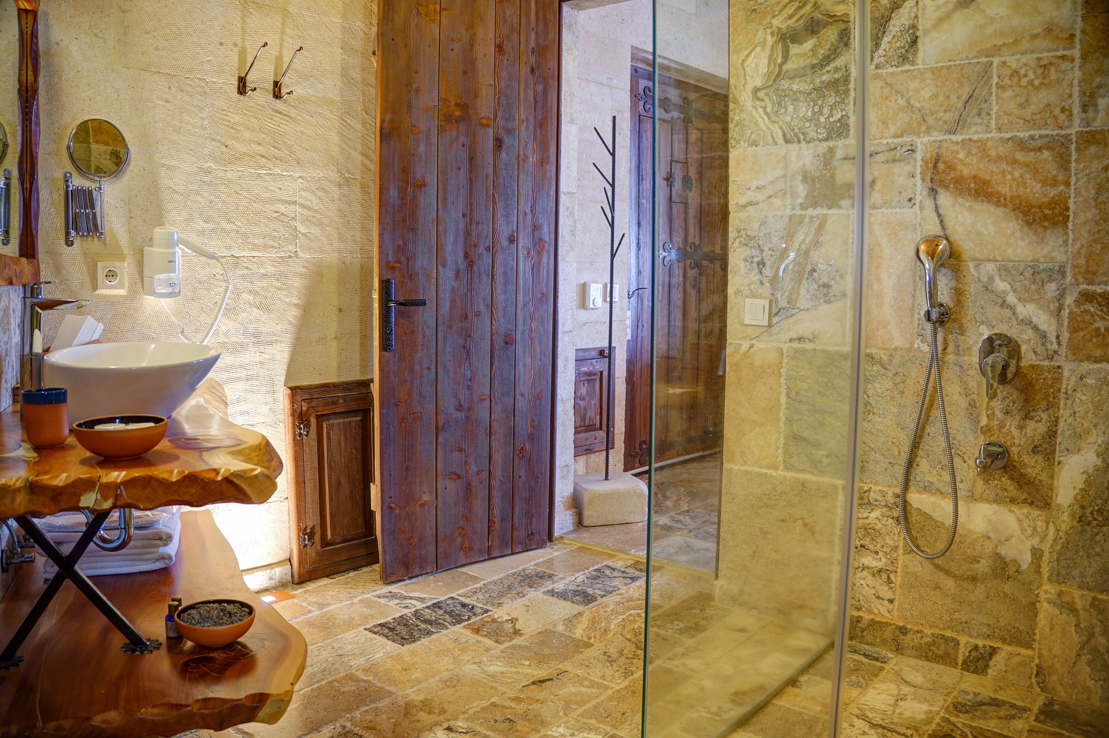 A bathroom with a wooden door, a glass shower enclosure, and a sink with a bowl.