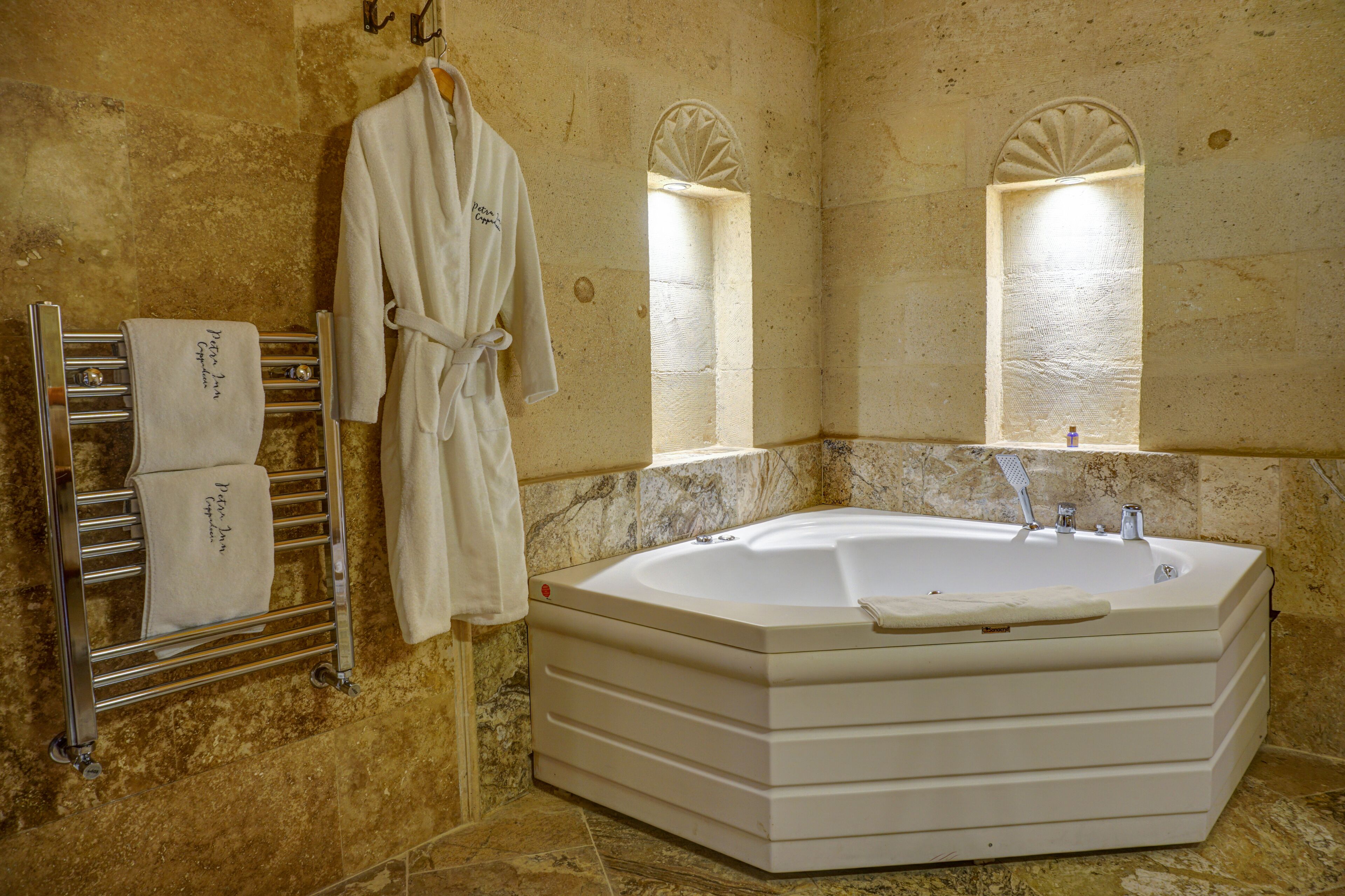 Une salle de bain avec une grande baignoire, un porte-serviettes avec des serviettes et deux fenêtres en arc de cercle.