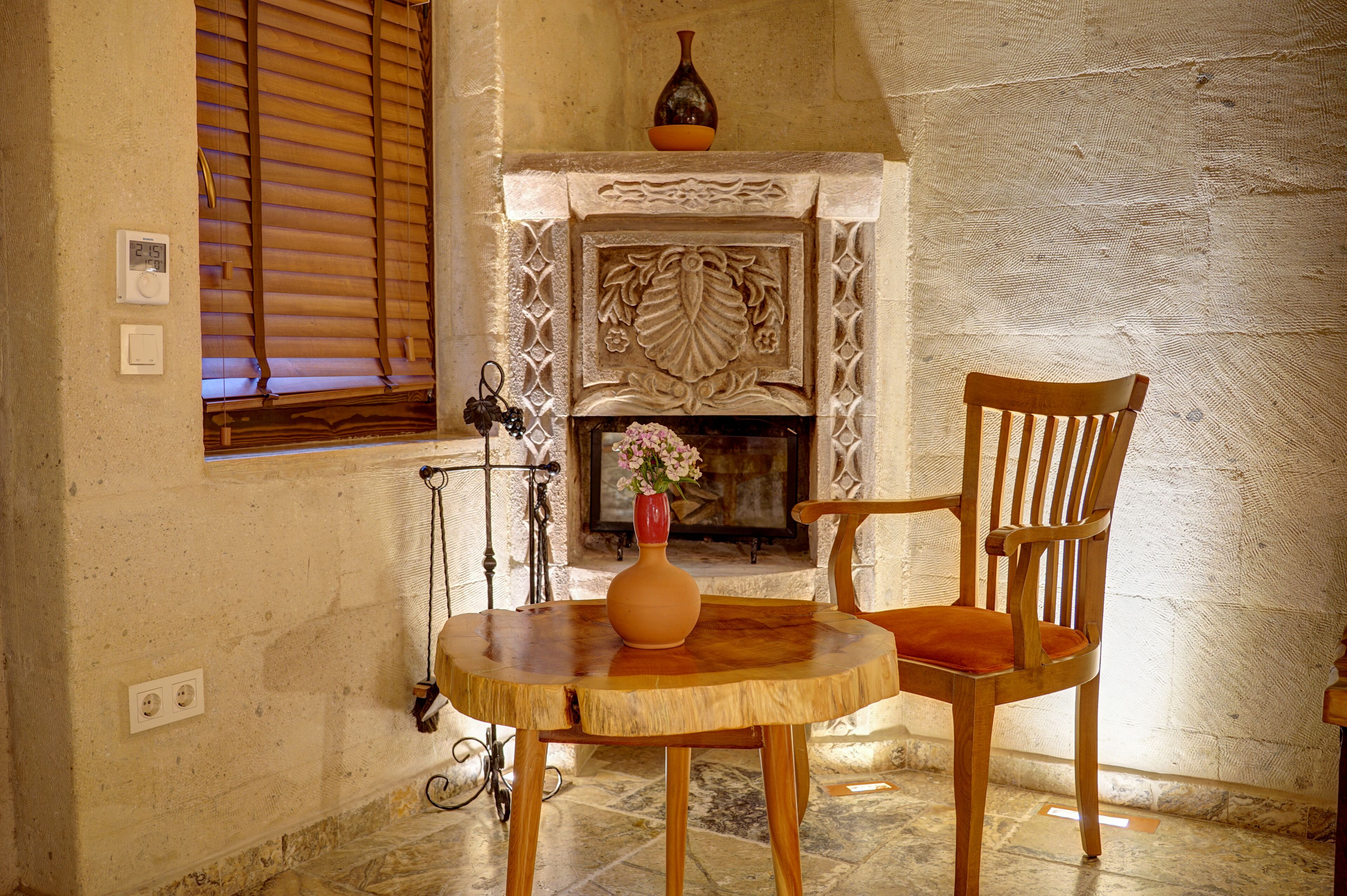 Une pièce avec une cheminée, une chaise en bois, une table ronde en bois et un vase rempli de fleurs.
