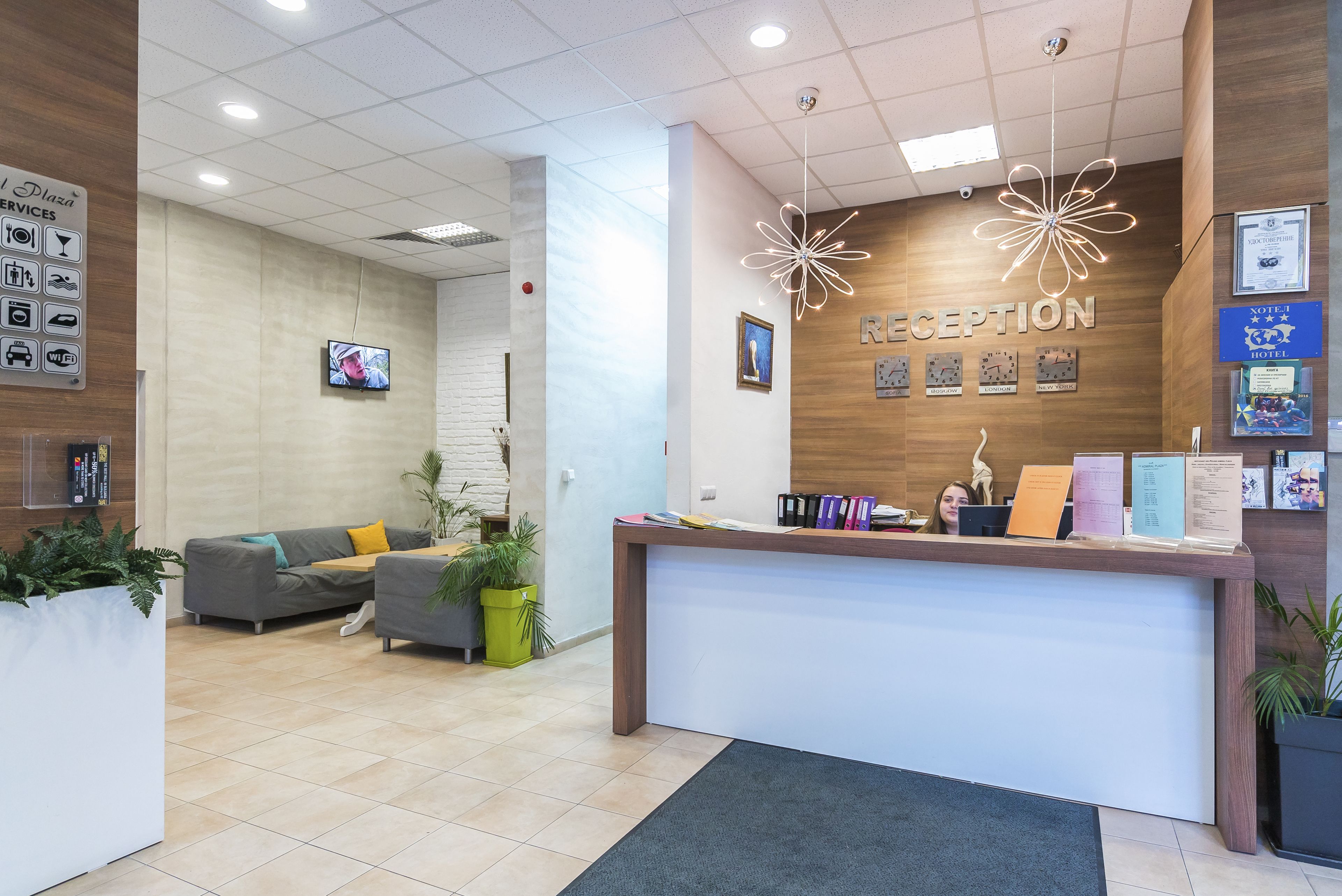 A reception area with a wooden reception desk, a grey sofa, and a TV screen.