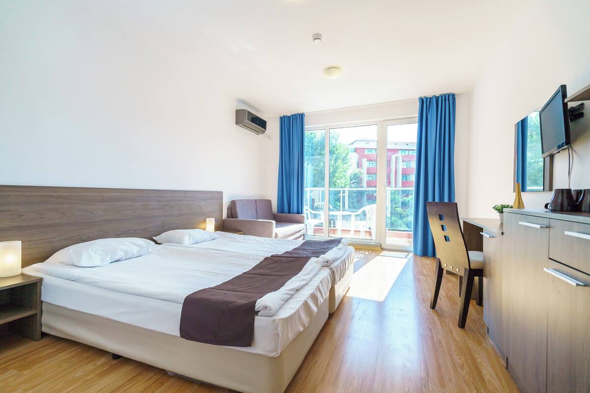 A hotel room with a large bed, a desk, a chair, and a TV.