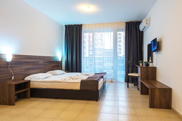 Ein Schlafzimmer mit einem Bett, Nachttischen, einem Fernseher und einem Fenster mit Vorhängen.