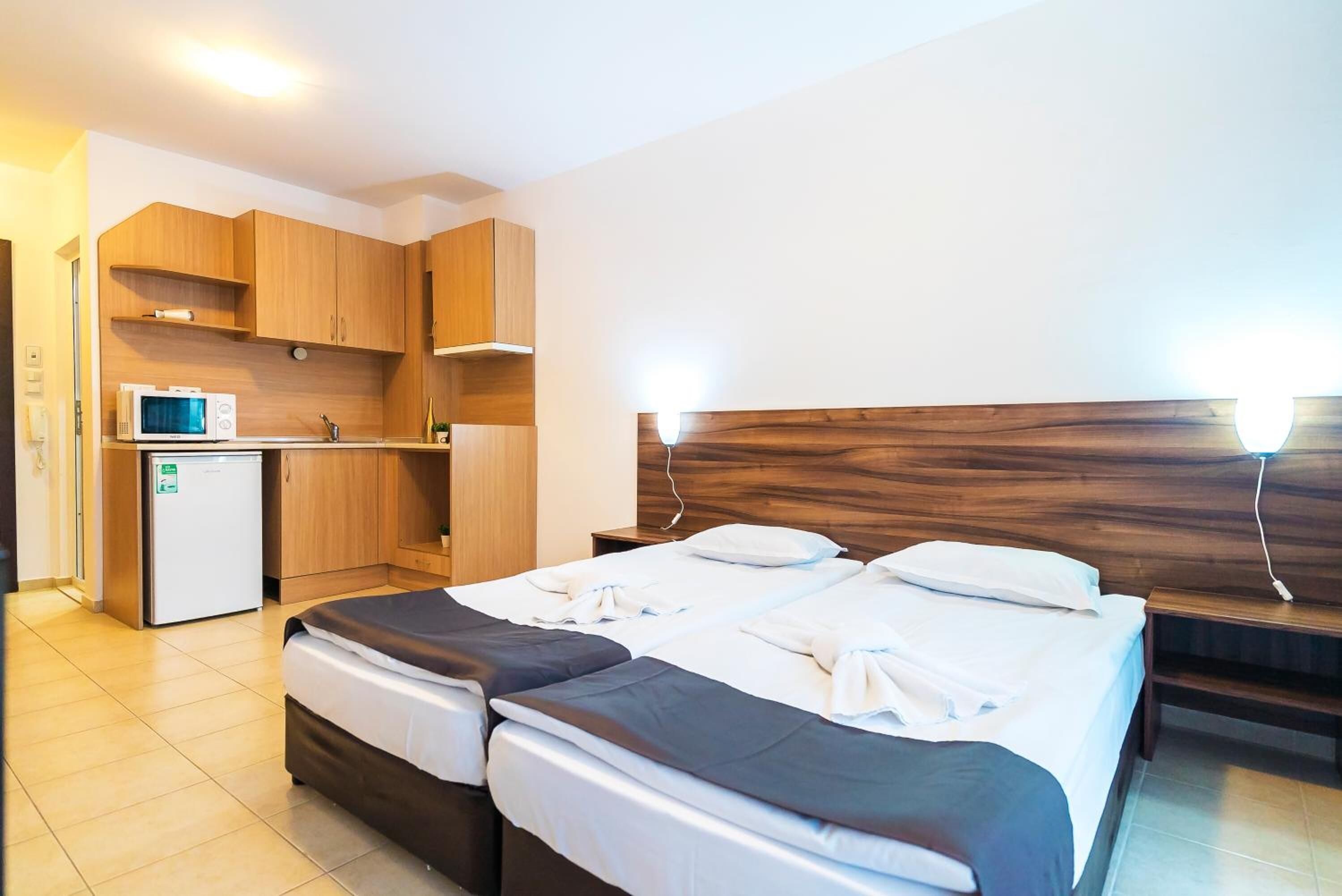 A hotel room with a bed, a small kitchenette, and a wooden headboard.