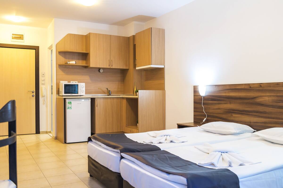 A hotel room with a bed, a desk with a microwave, a small fridge, wooden cabinets, and a wooden headboard.