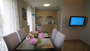 Un coin repas avec une table dressée pour quatre personnes, un vase de fleurs, une cuisine avec des meubles en bois et un téléviseur fixé au mur.