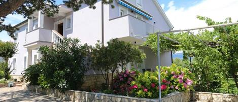 A two-story building with a stone wall garden, a pergola, and a clear sky.