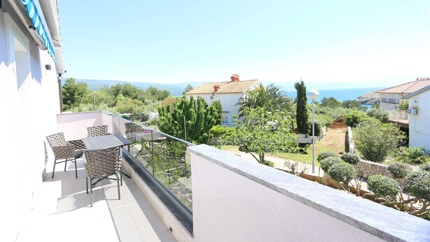 Un balcon avec une table et des chaises, donnant sur un quartier résidentiel avec des maisons et un ciel dégagé.