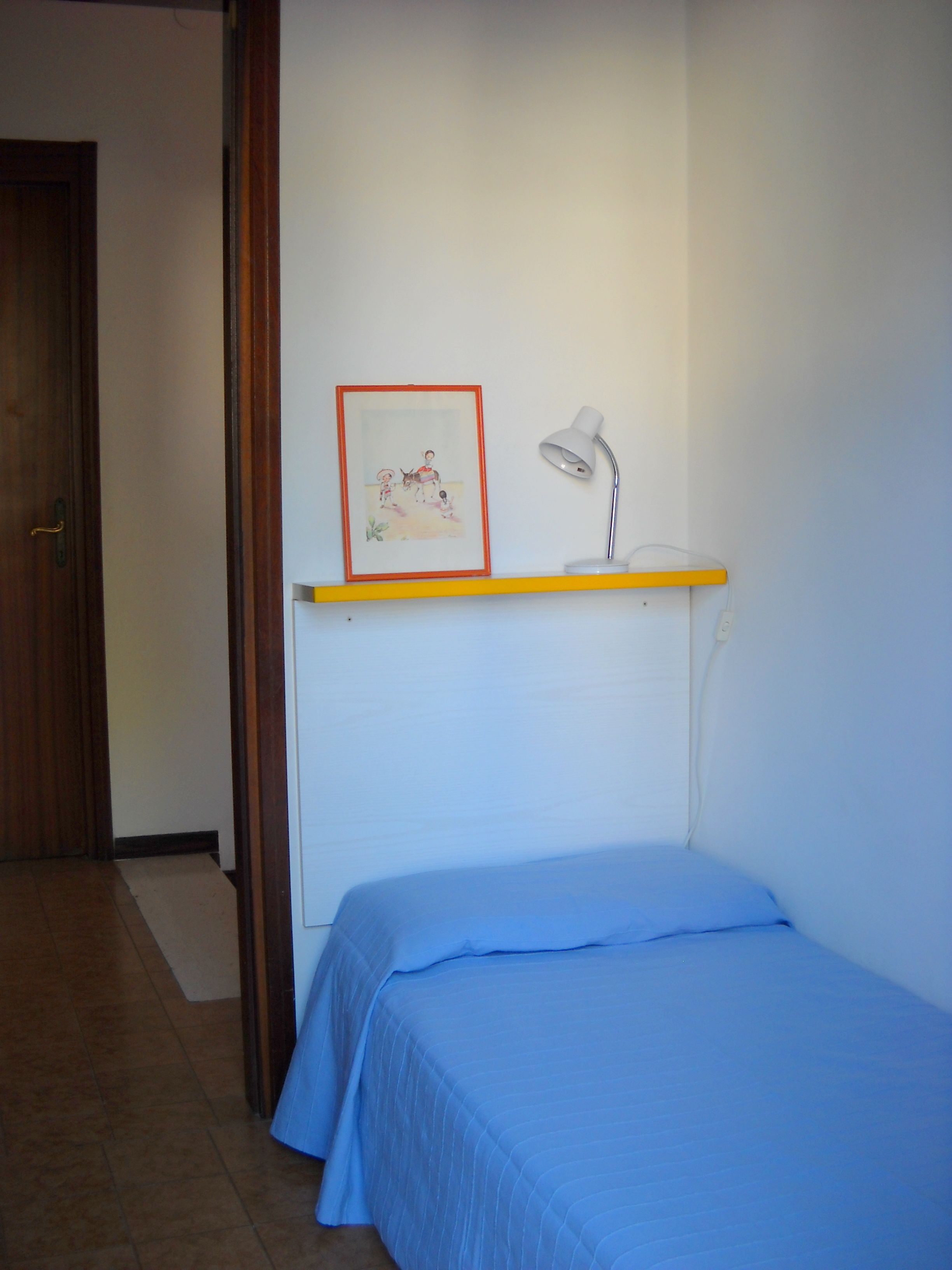 A bedroom with a single bed, a bedside table with a lamp, and a framed picture on the wall.