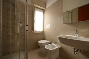 A bathroom with a glass shower enclosure, a toilet, a bidet, and a sink with a mirror above.