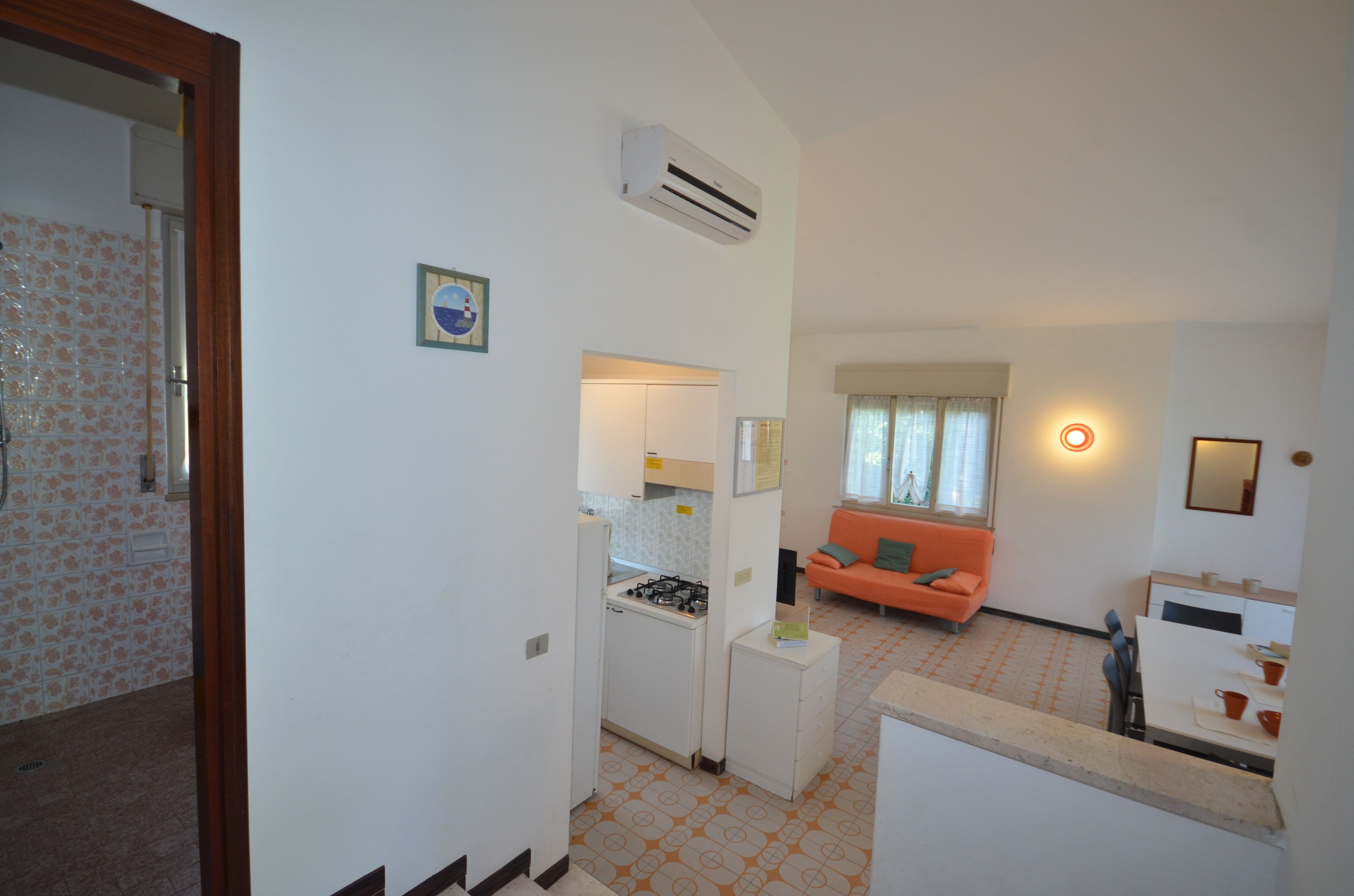 A compact living space with a kitchenette, a dining area, and a seating area with an orange sofa.