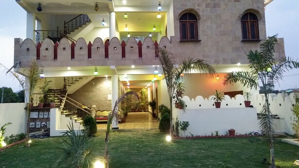 A multi-story building with a traditional architectural style, featuring a central staircase, multiple balconies, and a well-maintained garden with potted plants. - Hotel Vamdev Fort (Pushkar)