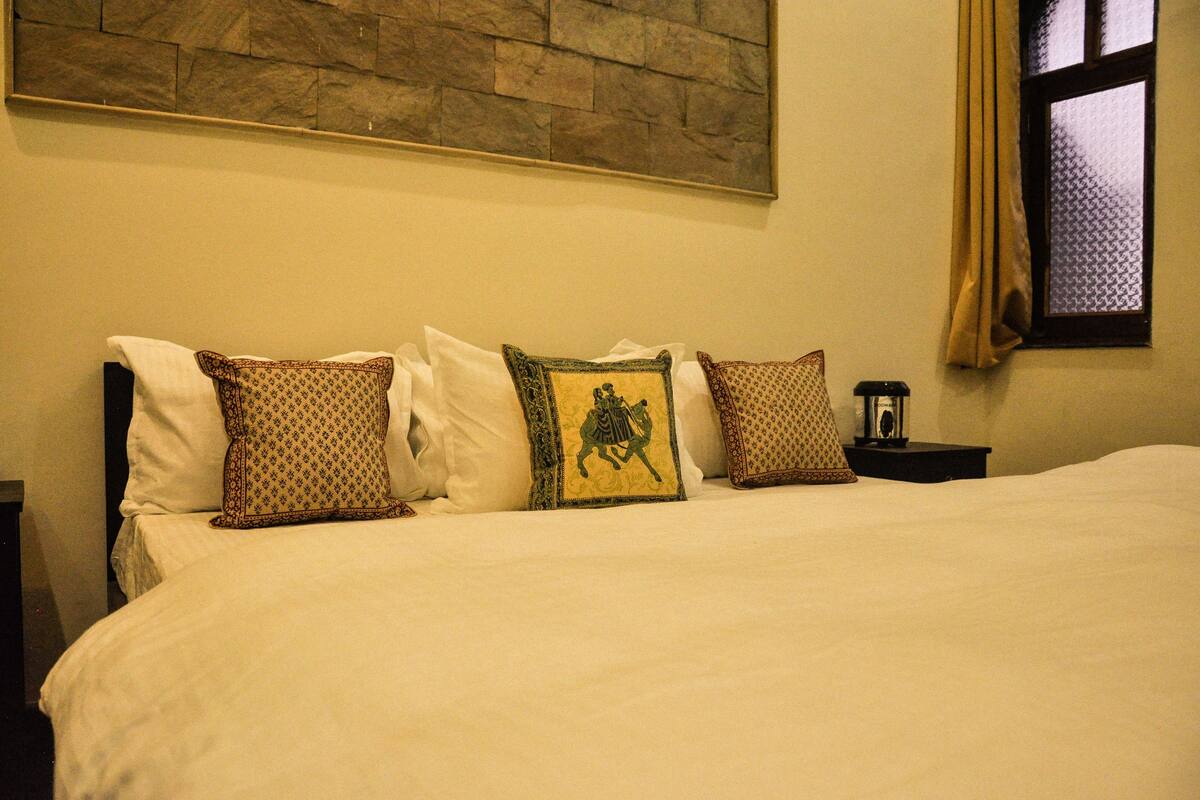 A neatly made bed with patterned pillows, a nightstand with a lamp, and a stone wall above.