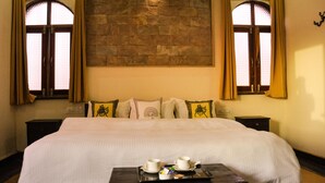 A hotel room with a large bed, two bedside tables, a tray with cups and a small box, and a stone wall behind the bed. - Hotel Vamdev Fort (Pushkar)