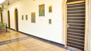 A hallway with art on the walls, a large door, and a tiled floor. - Hotel Vamdev Fort (Pushkar)