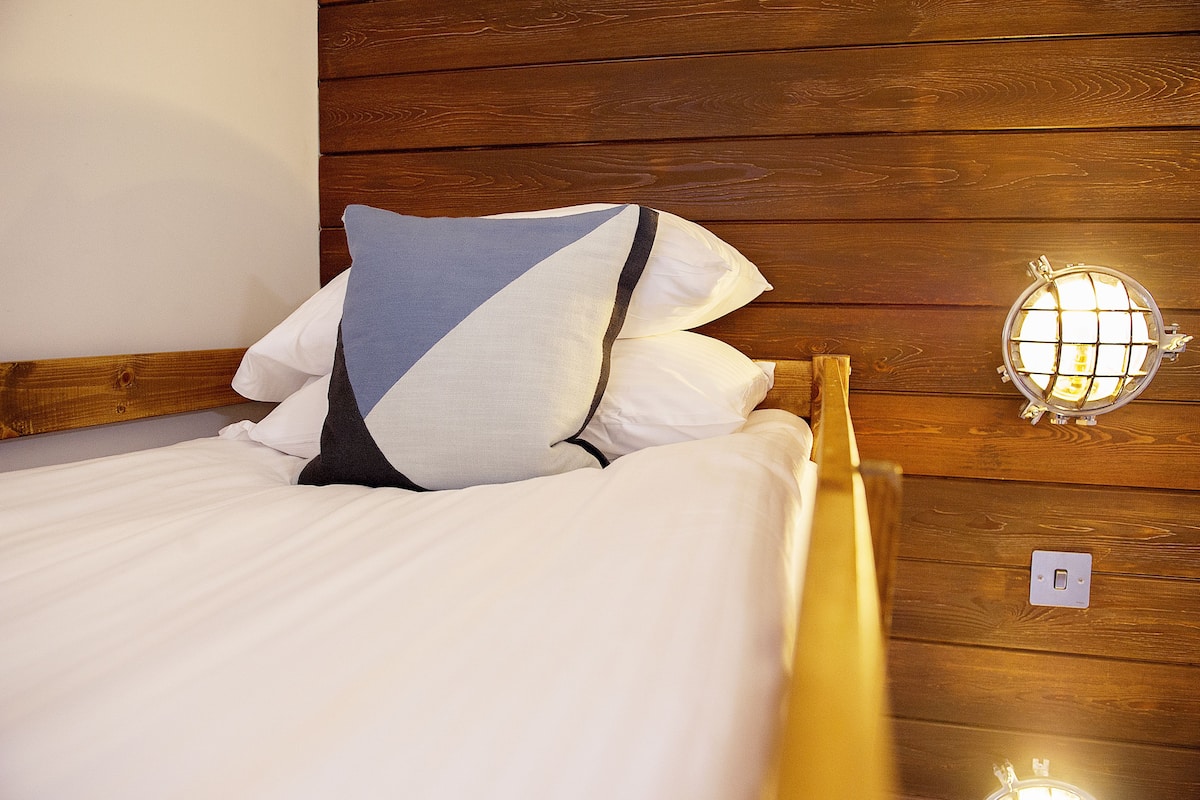 Una cama con ropa de cama blanca y un almohadón de estampado geométrico.
