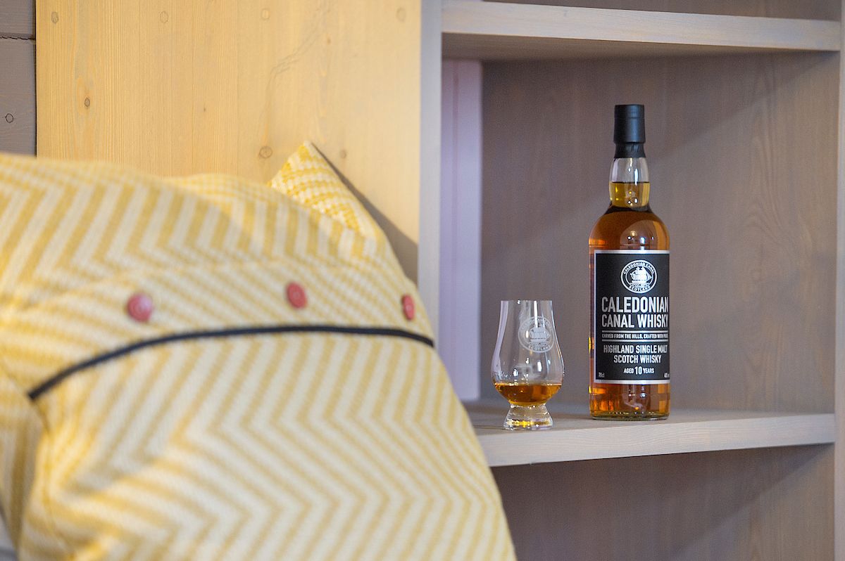 A bottle of Caledonian Canal Whisky and a glass on a shelf.