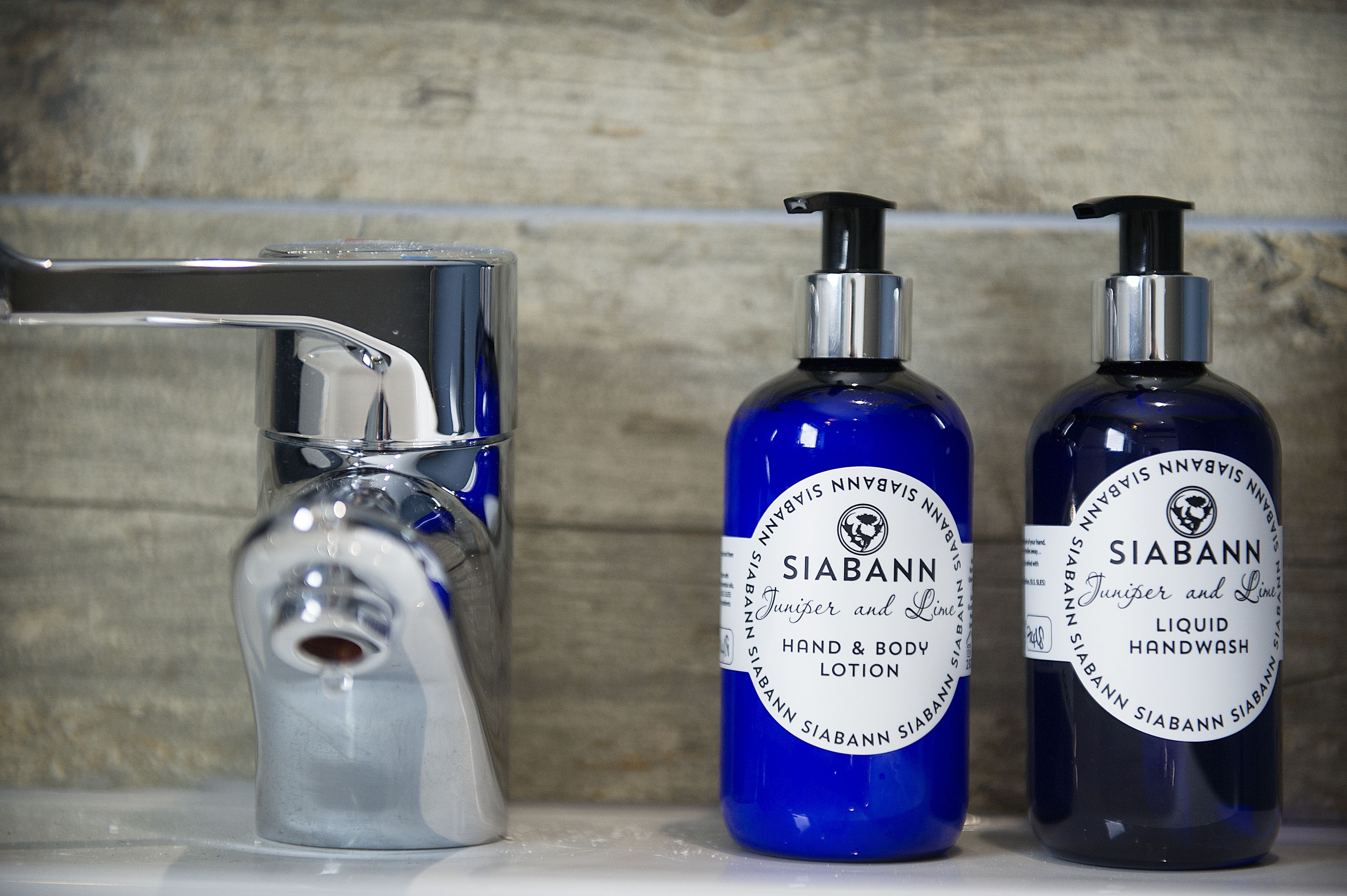 A bathroom with a chrome faucet and two bottles of Siabann hand and body lotion.