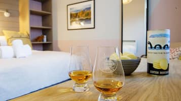 Deux verres de whisky sur une table en bois, dans une chambre d’hôtel. On aperçoit un lit et une bibliothèque à l’arrière-plan.