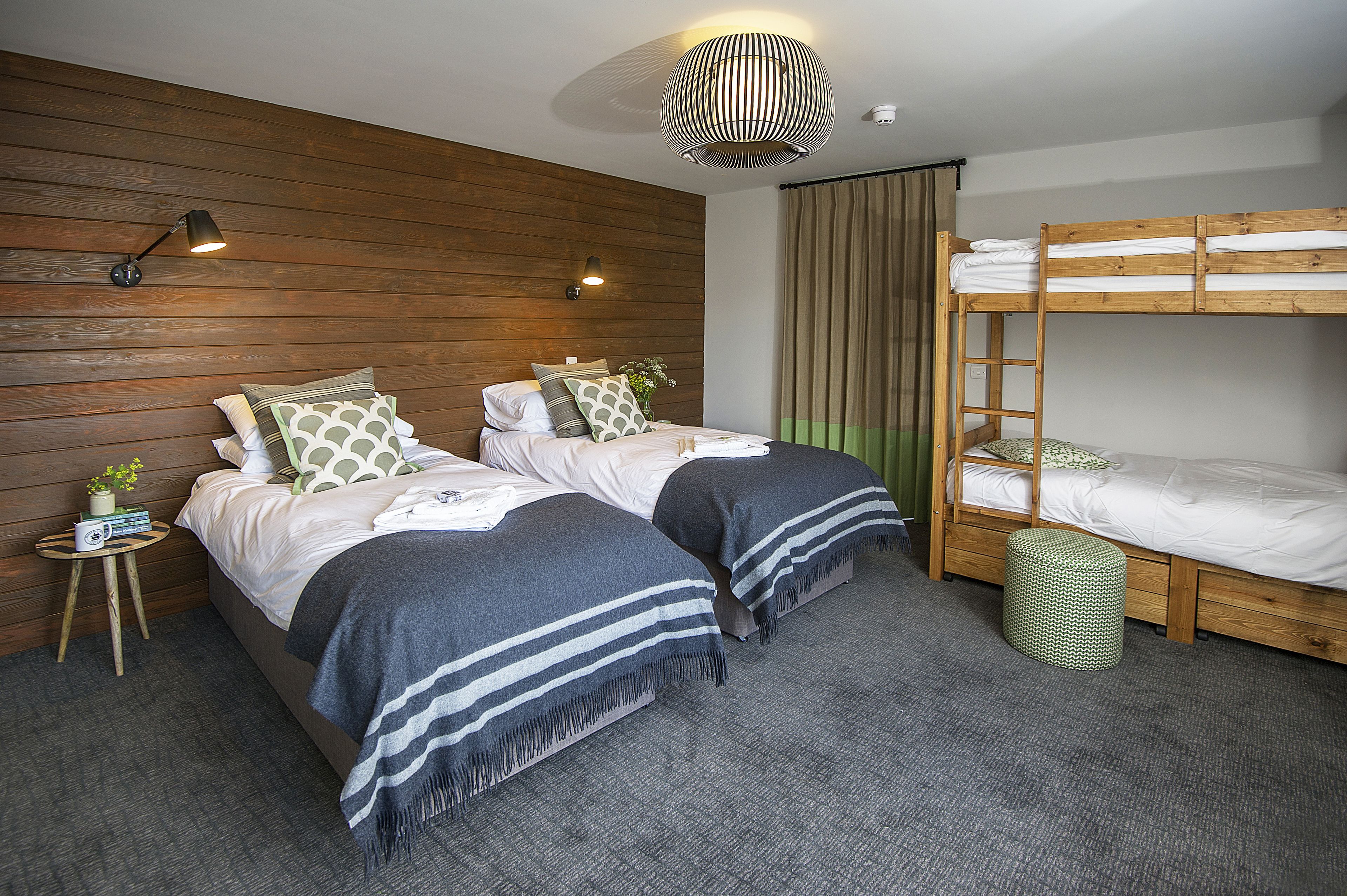 A room with two beds, a bunk bed, a small side table with a radio, and a hanging light fixture.