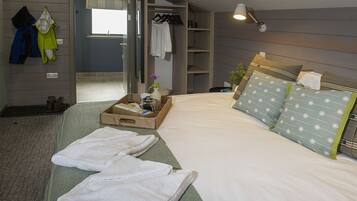A hotel room with a bed, a wooden wardrobe, a mirror, and a small table with a vase and a box.