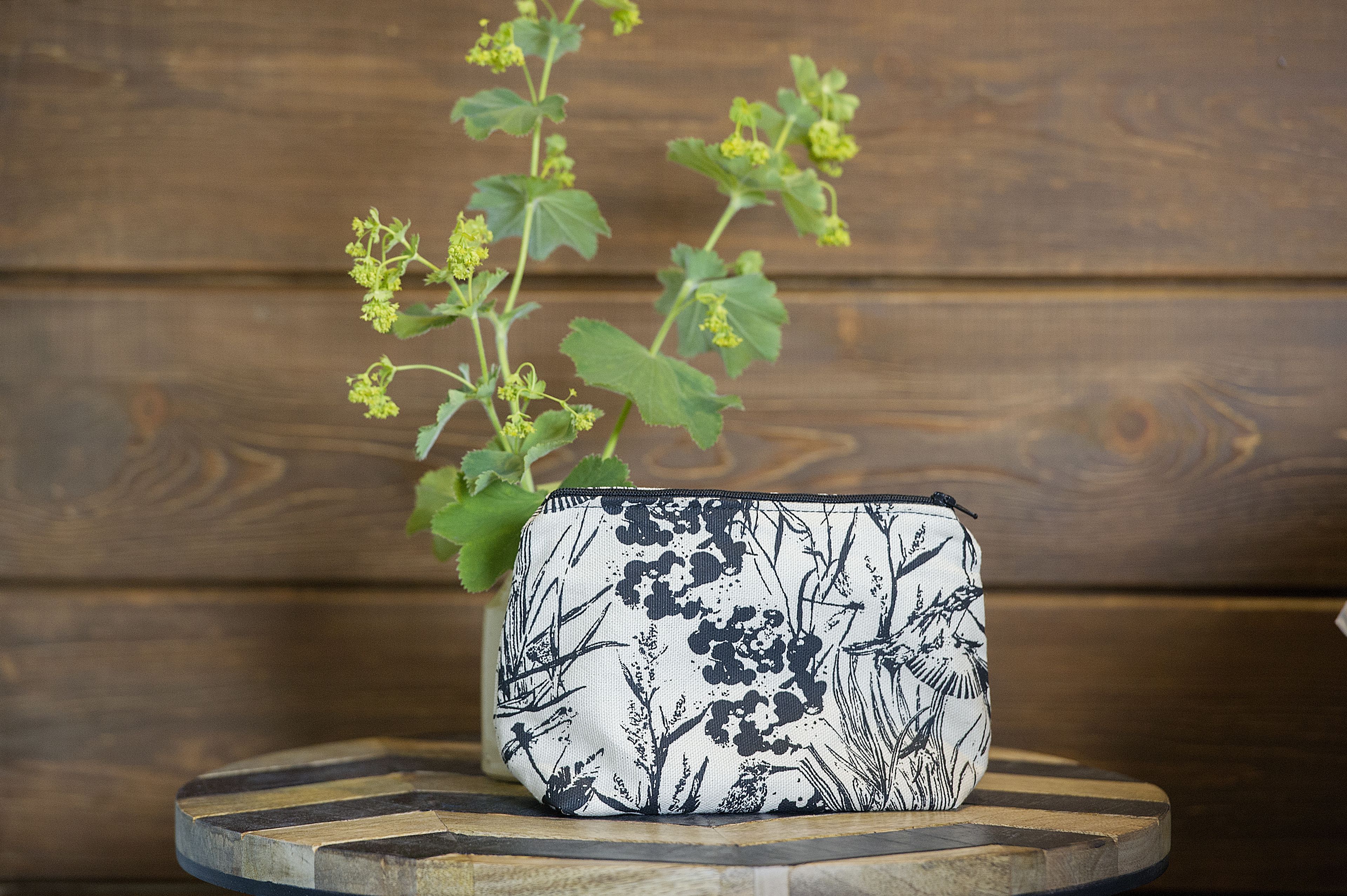 Una mesita pequeña y redonda de madera con un bolso blanco y negro estampado encima.