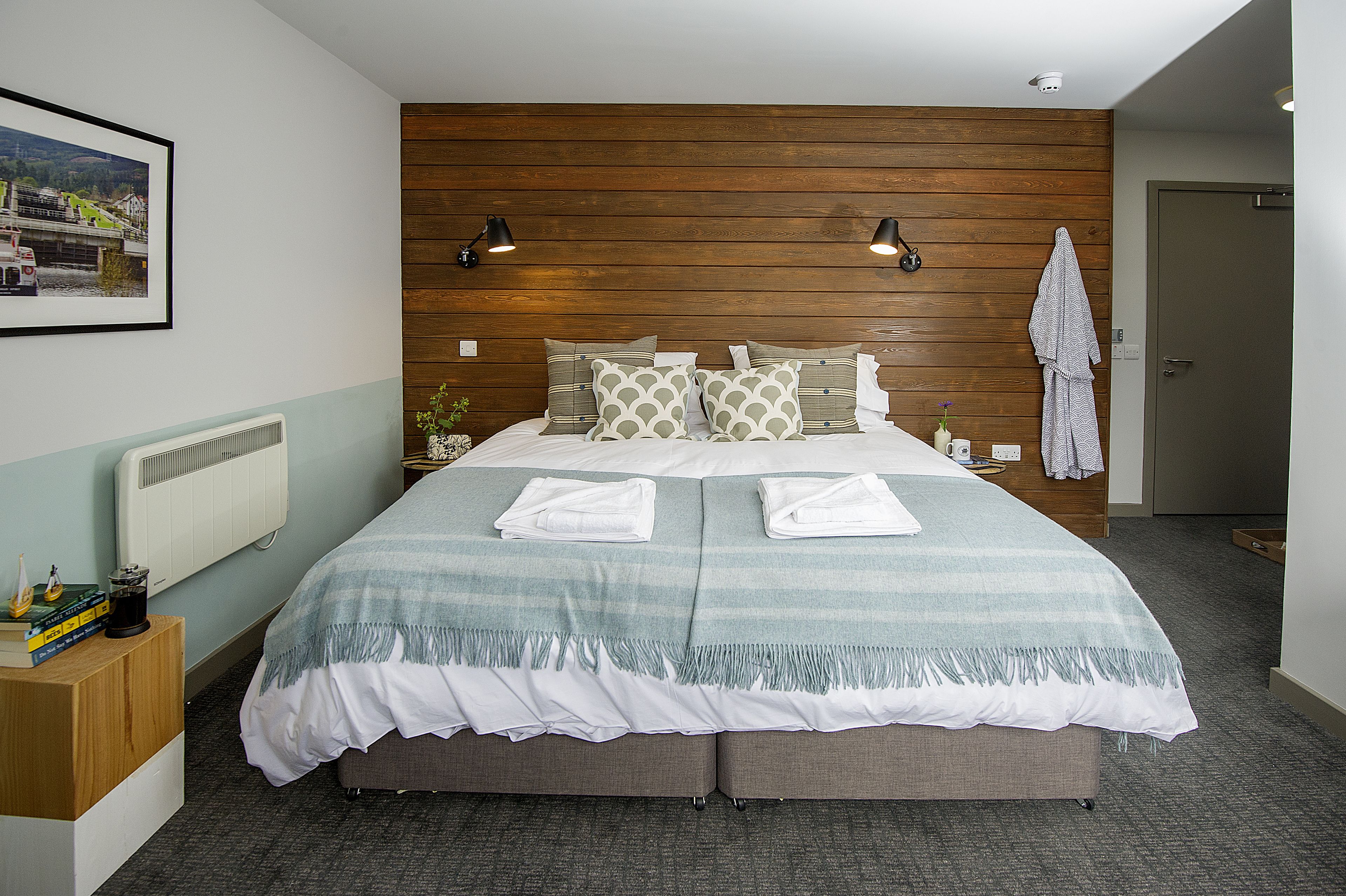 A neatly made double bed with a striped blanket, two bedside lamps, and a framed picture on the wall.