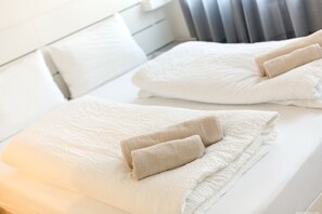 A neatly made bed with white linens and two beige towels folded at the head. - Apartment Terme (Merano)
