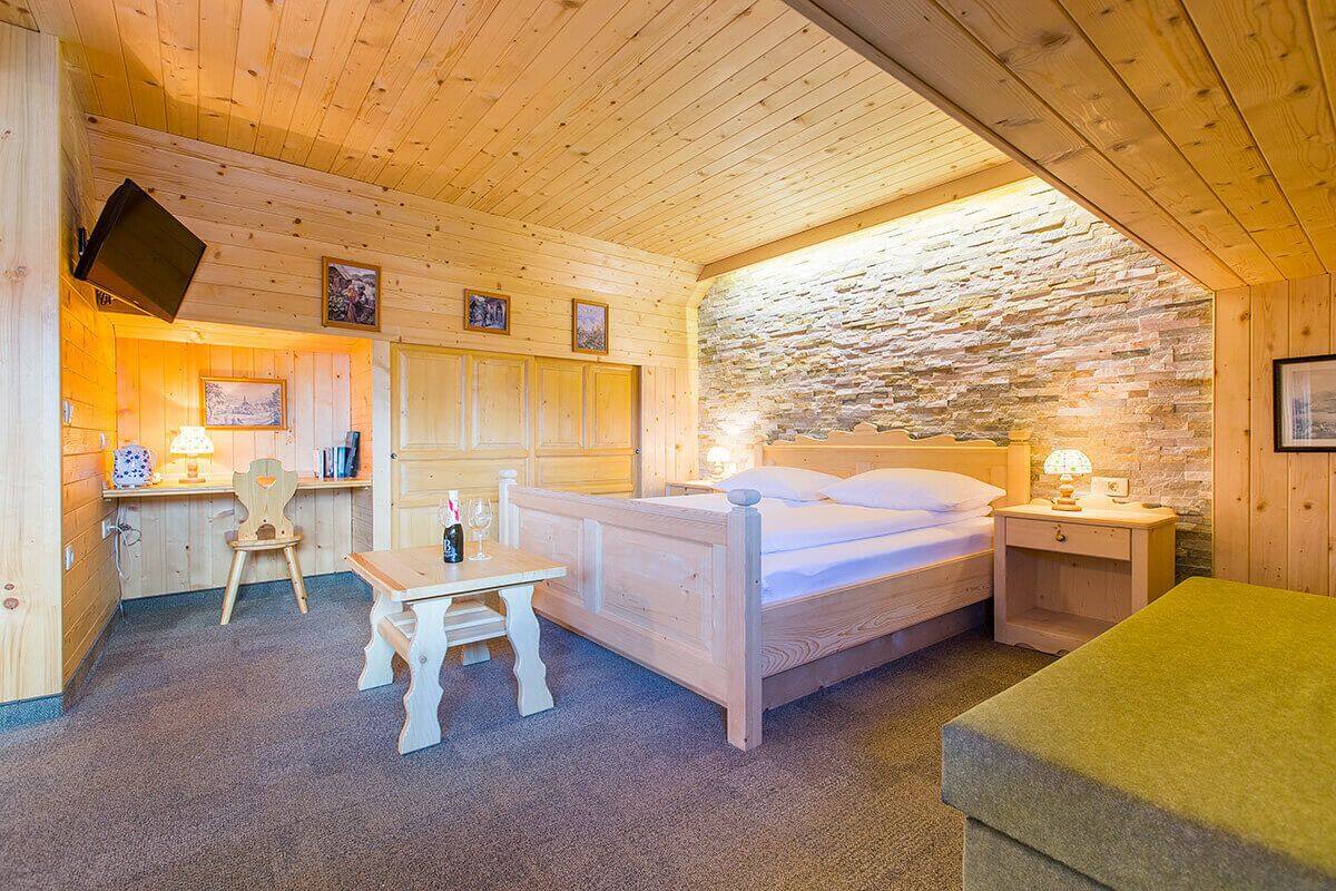 A cozy wooden room with a bed, a desk, and a stone wall.