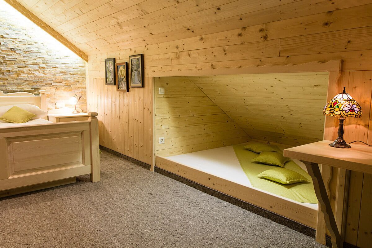 Una habitación acogedora con techo inclinado, cama con ropa de cama verde, mesita de noche con lámpara y pared de piedra.