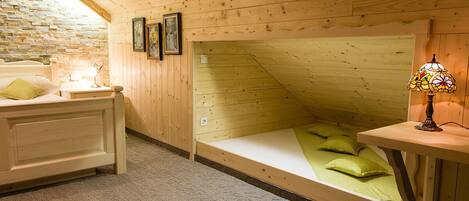 Una habitación acogedora con techo inclinado, cama con ropa de cama verde, mesita de noche con lámpara y pared de piedra.