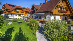 A traditional chalet-style building with a sloped roof, wooden balconies with flower boxes, and a well-maintained garden with tables and chairs.